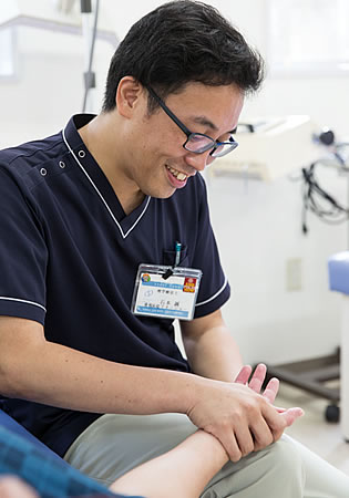 写真:ベッドに寝ている男性の患者さんとその奥に座っている石本さん。