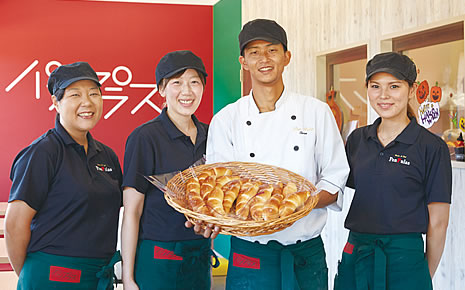 写真:中央には、平たい大きなカゴに入ったパンを持っている大久保さん夫妻。両脇には従業員の女性が1名ずつ並んで立っている。